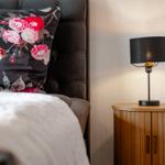 Schlafzimmer mit Bett, Kissen mit Blumenmuster und Nachttisch mit Lampe.