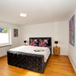 Schlafzimmer mit Bett, Nachttischen und Fenster. Holzboden und Wandbilder.