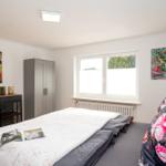 Schlafzimmer mit Bett, Kleiderschrank und Fenster. Wandbilder und Zeitschrift auf Bett.