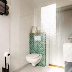 Badezimmer mit Toilette, Waschbecken und grüner Fliesenwand.