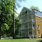 Gelbes Mehrfamilienhaus mit weißen Balkonen und umliegenden Bäumen.