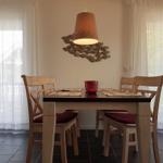 Esszimmer mit Holztisch, vier Stühlen und Deckenleuchte. Fenster mit weißen Vorhängen.