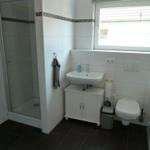 Badezimmer mit Dusche, Waschbecken und Toilette. Fenster sorgt für Tageslicht.