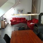 Wohn- und Essbereich mit rotem Sofa, Esstisch und Kaminofen unter Dachschrägen.