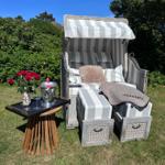 Strandkorb mit Kissen und Fußstützen auf Gras. Tisch mit Rosen und Champagner.