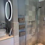 Badezimmer mit Dusche, Waschbecken und beleuchtetem Spiegel