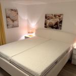 Schlafzimmer mit Doppelbett, zwei Nachttischen und Wandbildern mit Muscheln.