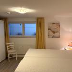Schlafzimmer mit Bett, Nachttisch, Lampe und Fenster mit gelben Vorhängen.