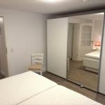Schlafzimmer mit Bett, Stuhl und Schiebetüren. Spiegel reflektiert weitere Räume.
