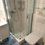 Badezimmer mit Dusche, Waschbecken und WC. Fliesenboden und weiße Wände.