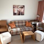 Wohnzimmer mit Sofa, Sesseln und Tisch. Wandbild und Fenster mit Vorhängen.