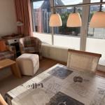 Ein Essbereich mit Tischdecke und Stühlen, daneben Wohnbereich mit Sofa und Sessel.