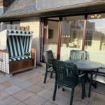 Terrasse mit Strandkorb und Tisch mit Stühlen vor Haus mit Glasfront.