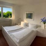 Schlafzimmer mit Doppelbett, Fenster und Blumenvase.