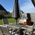 Terrasse mit Tisch, vier Stühlen und geschlossenem Sonnenschirm. Im Hintergrund Strandkörbe und Grünfläche.