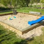 Ein Sandkasten mit blauer Rutsche und Spielzeug im Garten.
