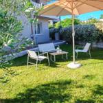 Garten mit Sonnenschirm, drei Stühlen und Tisch. Grasfläche, Baum und Hecke im Hintergrund.