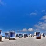 Strand mit blau-weißen Strandkörben unter blauem Himmel mit weißen Wolken.
