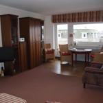 Wohnraum mit Fernseher, Schränken, Sitzgruppe und Fensterblick.