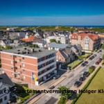Aerial view of a coastal town with houses, streets, and the sea in the background.