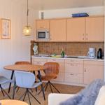 Küche mit Holzschränken, Esstisch und Stühlen. Hintergrund: Fliesenwand und Mikrowelle.