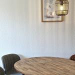 Runder Holztisch mit Stühlen unter einer Pendelleuchte an der Wand.