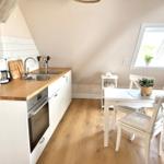 Küche mit Essbereich unter Dachschrägen. Holzfußboden, weiße Möbel und Fenster.