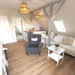 Wohnbereich mit Sofa, Sessel, Esstisch und Küchenzeile unter Holzbalken.