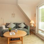 Wohnzimmer mit Sofa, Tisch und Blick auf Balkon mit Stuhl.