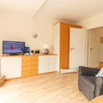 Wohnzimmer mit Sofa, TV und Holzboden. Tür führt in andere Räume.