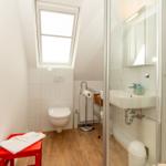 Badezimmer mit Dusche, Waschbecken und Toilette unter Dachschräge mit Fenster.