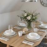 Ein gedeckter Holztisch mit weißen Geschirr und Blumendekoration.