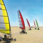 Sailbikes auf Sand mit bunten Segeln unter blauem Himmel.