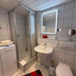 Bad mit Toilette, Dusche und Waschbecken mit beleuchtetem Spiegel.