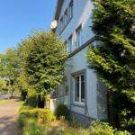 Ein zweistöckiges Haus mit Fenstern und einem Satellitenschüssel. Umgeben von Bäumen und Grünflächen.