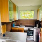Küche mit Holzschränken, Edelstahlgeräten und Fenster zur grünen Außenseite.