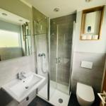 Badezimmer mit Dusche, Waschbecken und Toilette. Graue Fliesen und Spiegel.