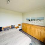 Schlafzimmer mit Bett, Holzschrank und Strandbildern an der Wand.