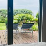 Durch die Glastür blickt man auf eine Terrasse mit zwei Liegestühlen und einen grünen Garten.