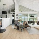 Living area with fireplace, leather sofa, and wooden floor. Large windows and white ceiling.
