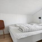 Bedroom with bed, brown chair, and window. White walls and wooden floor.