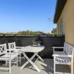 Terrace with white table and chairs, closed umbrella, and view of green areas.