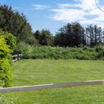 Green lawn area with wooden fence and forest in background under blue sky.