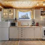 Kitchen with white cabinets, refrigerator, stove, and window with view of trees.