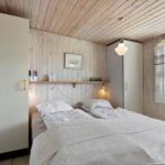 Bedroom with wooden walls, bed, wardrobe, and window with view.