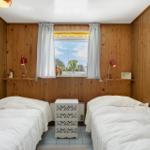 Two beds with white sheets, wooden walls, window with view outside, and nightstand.