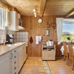 Kitchen with dining area, wooden walls, and windows. Kitchen counter, table, chairs, appliances.