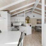 Kitchen with dining area and living room in background. Wooden ceiling and light interior.