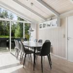Dining area with table and chairs, large window to terrace, wood wall and white ceiling.