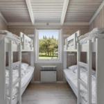 Room with two bunk beds, wooden walls, and window view of green area.